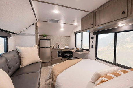 An inviting RV rental interior, showcasing a well-equipped kitchen, comfortable bed, and living area with scenic windows.