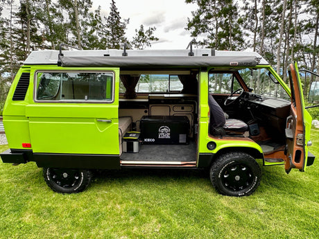 Vibrant green camper van RV rental, side open. Features ARB awning, ICECO cooler, and off-road tires for adventure.