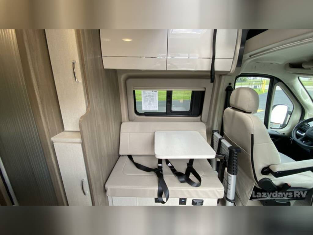 Interior of an RV rental: a beige dinette with removable table, overhead cabinets, and front passenger seat.