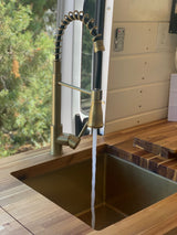 RV rental kitchen: modern brass faucet pouring water into a matching sink, surrounded by warm wood countertops.