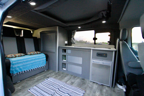 Spacious RV rental interior featuring a convertible bed, compact kitchen area, and storage cabinets. Perfect for travel.
