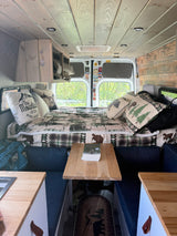 Cozy RV rental camper van interior: nature-themed bed, wooden ceiling/walls, kitchen, and dining nook for comfortable travel.