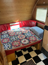 Cozy RV rental interior with a patchwork quilt bed, red cushions, wood paneling, and checkered floor. Perfect for a road trip!