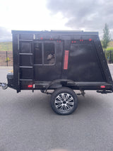 Explore with this compact black adventure trailer, perfect for RV rental. Features a window, wheel, and reflective accents.