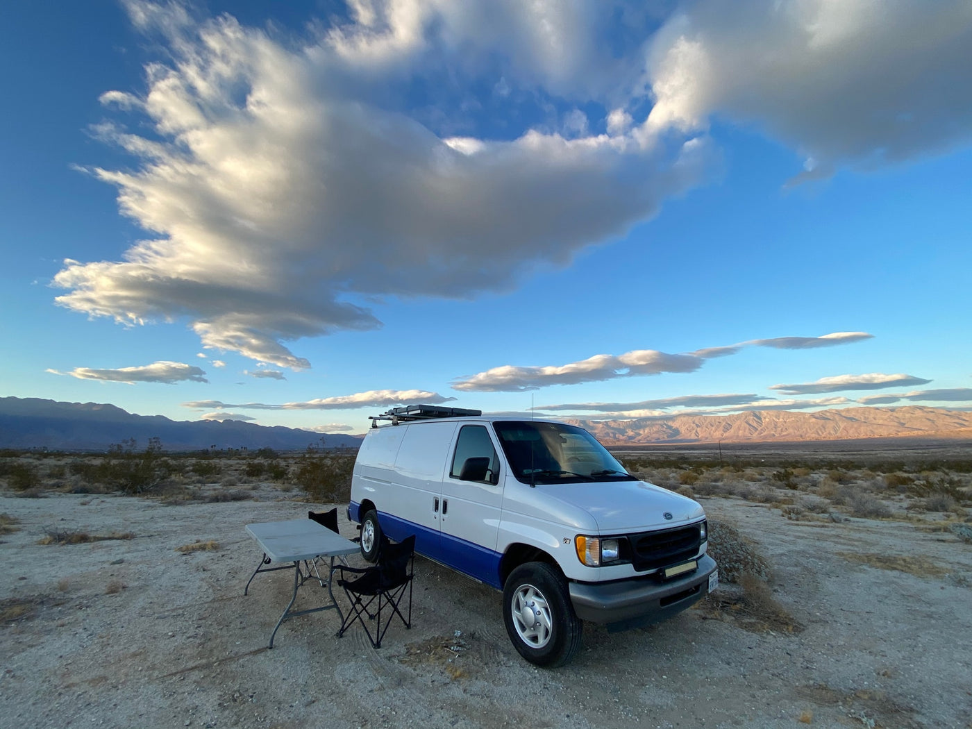This adventure-ready camper van, available for rv rental, is set up for desert camping with a table and chairs under a stunning cloudy sky. — photo 10