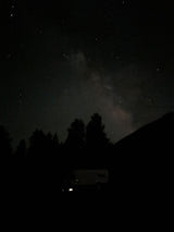 Stargazing from an RV rental under the Milky Way. Dark night sky with silhouetted trees & parked van.