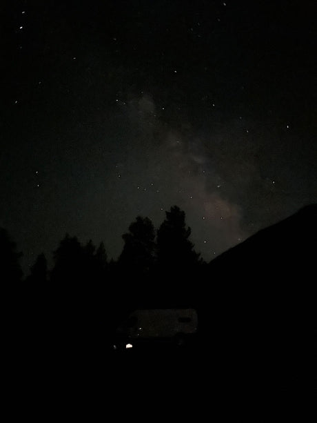 Stargazing from an RV rental under the Milky Way. Dark night sky with silhouetted trees & parked van.