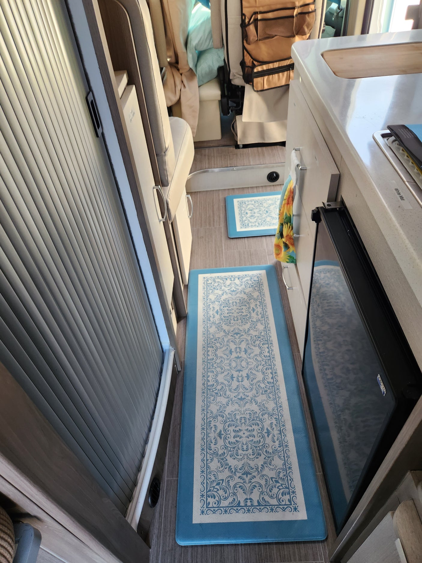 rv rental: Modern interior featuring a compact kitchenette, sleeping area, decorative blue floor mats, and tambour storage.