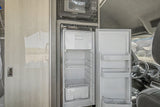 RV rental interior: An open refrigerator and microwave in a camper van's compact kitchen, with a glimpse of the outdoor landscape.