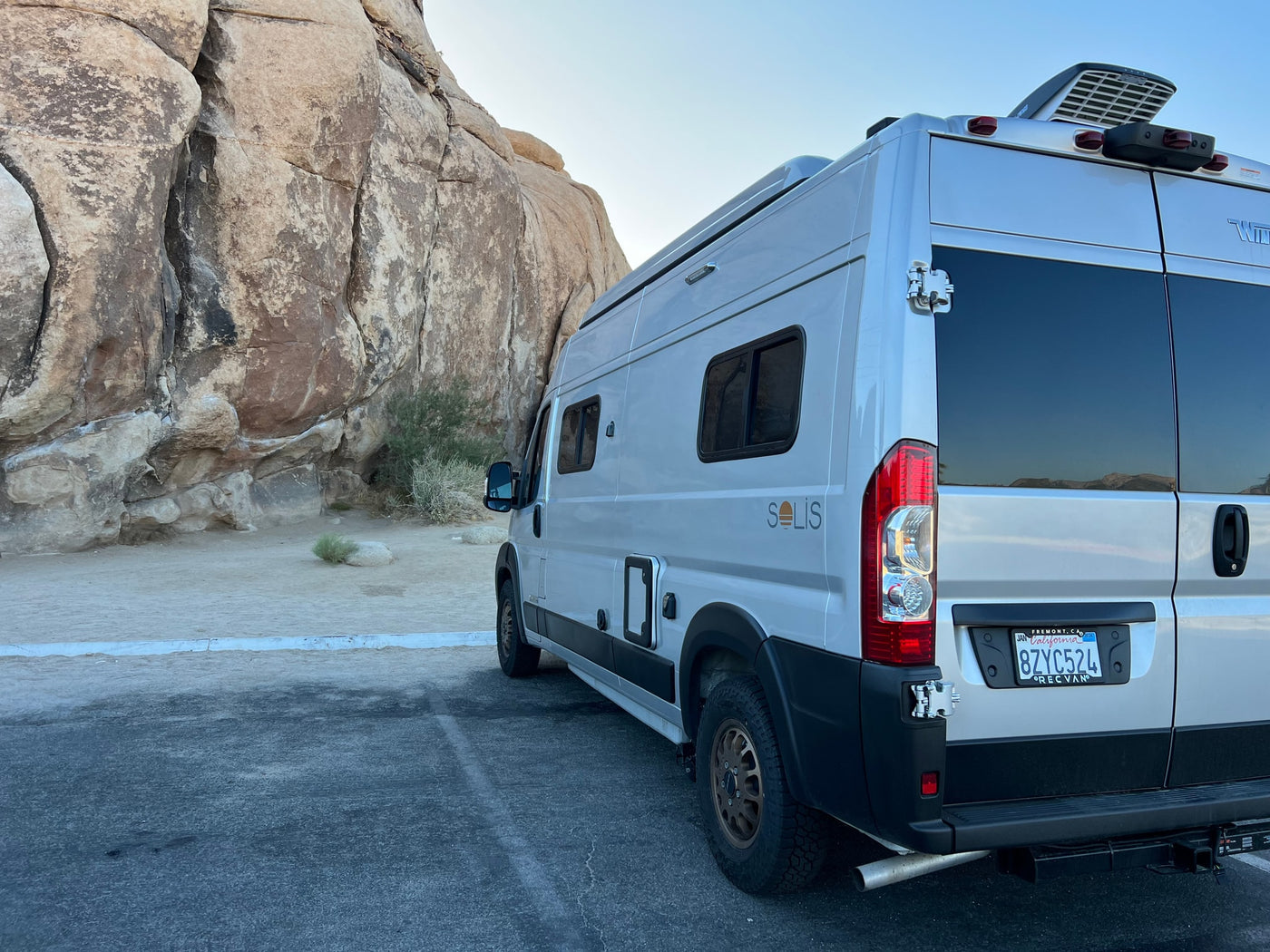 This rv rental Winnebago Solis camper van is parked by large desert rocks, ready for adventure. — photo 12