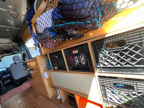 This RV rental showcases a well-organized camper van interior with custom wood shelving, crates, and an overhead storage net.