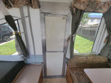 Interior of an rv rental pop-up camper, featuring a green mattress, patterned seating, and central door.
