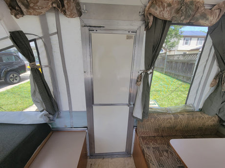 Interior of an rv rental pop-up camper, featuring a green mattress, patterned seating, and central door.