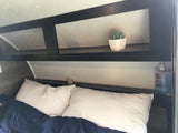 An RV rental's cozy bedroom features a bed with white pillows & blue blanket, plus overhead storage with a plant & Purell.