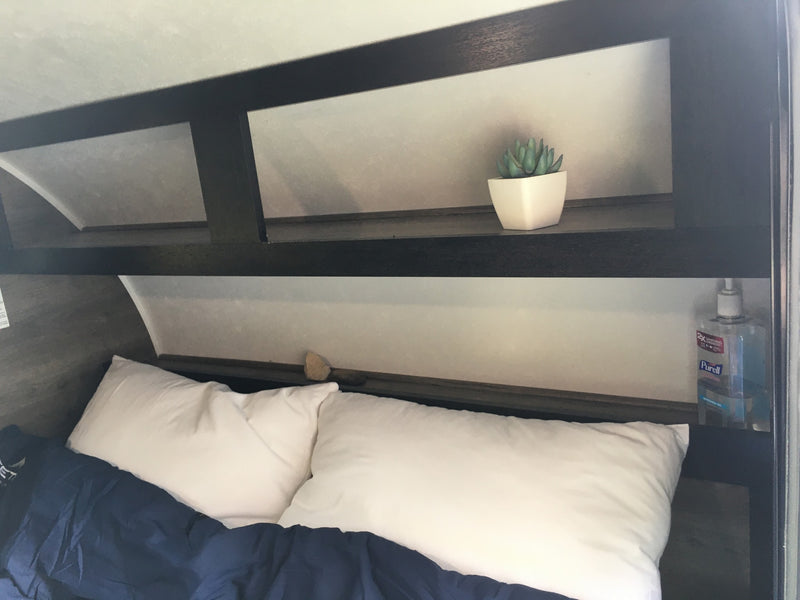 An RV rental's cozy bedroom features a bed with white pillows & blue blanket, plus overhead storage with a plant & Purell. — photo 6