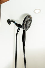 Black shower head and flexible handheld sprayer in an RV rental bathroom, with ceiling light.
