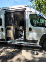 Winnebago Solis RV rental: A happy dog inside a cozy camper van, parked outdoors with its side door open for adventure.