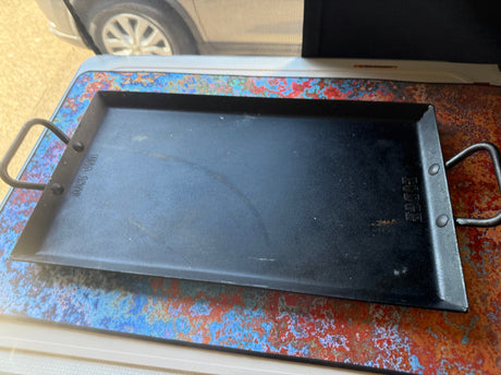 Lodge griddle on a vibrant mat, ready for cooking on your rv rental trip. View of RV window and tire.
