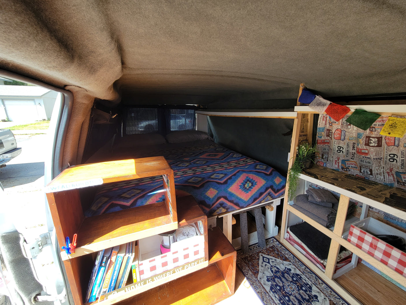Inside a custom RV rental: a warm, cozy interior with a comfy bed, storage shelves, and decorative prayer flags.