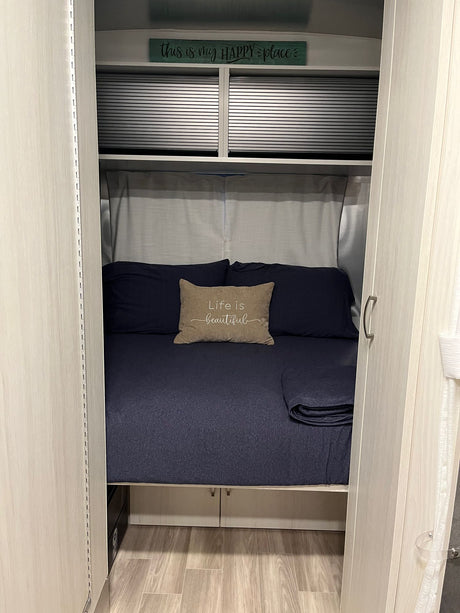 RV rental: View of a compact bedroom featuring a dark blue bed, "Life is beautiful" pillow, and overhead cabinets.