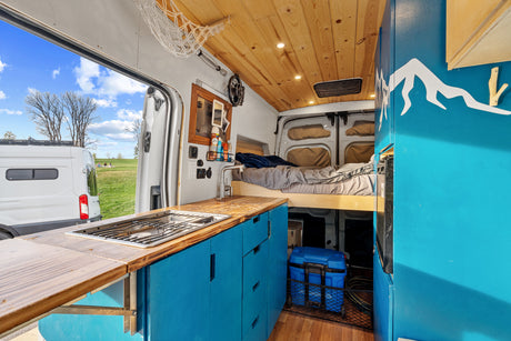 Stylish rv rental camper van interior: blue kitchen, wood ceiling, cozy bed, & park view perfect for van life adventures.
