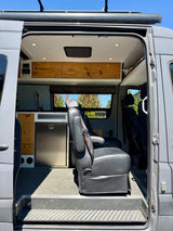Explore this custom RV rental interior: modern camper van with built-in fridge, wood cabinetry, and swivel seating.