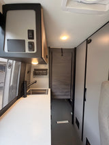 This RV rental interior features a modern galley kitchen with a black sink and faucet, overhead controls, and ample storage.