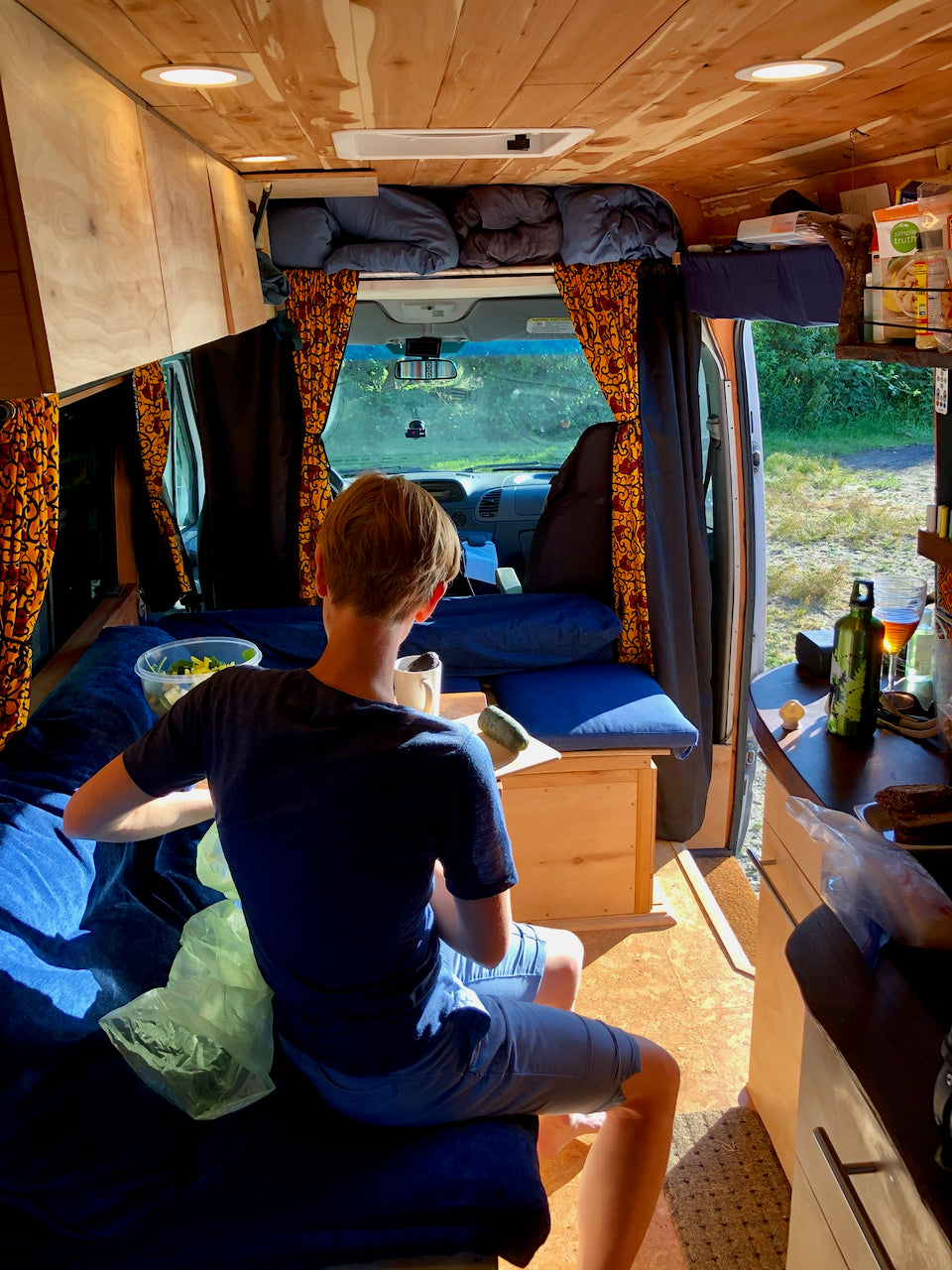 Cozy RV rental home. A person sits inside a converted van, enjoying the bright interior and view, showcasing comfortable van life.