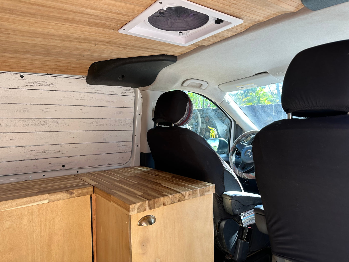 RV rental interior looking forward: detailed view of wooden ceiling, overhead fan, and custom wood cabinetry in a camper van. — photo 11