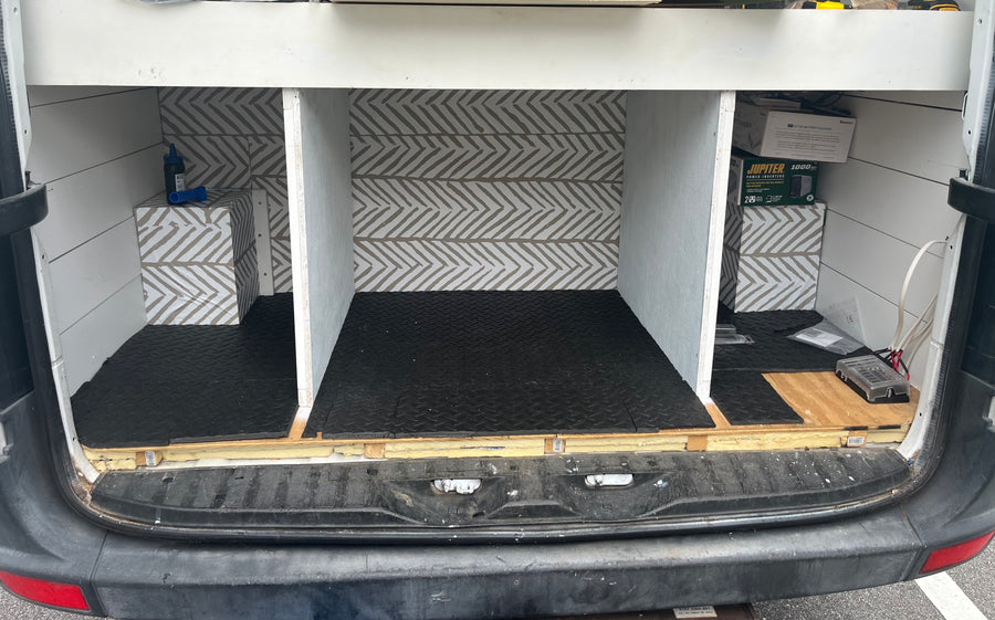 RV rental van's custom interior: organized cargo space with chevron walls, rubber mats, built-in storage, and power system setup.