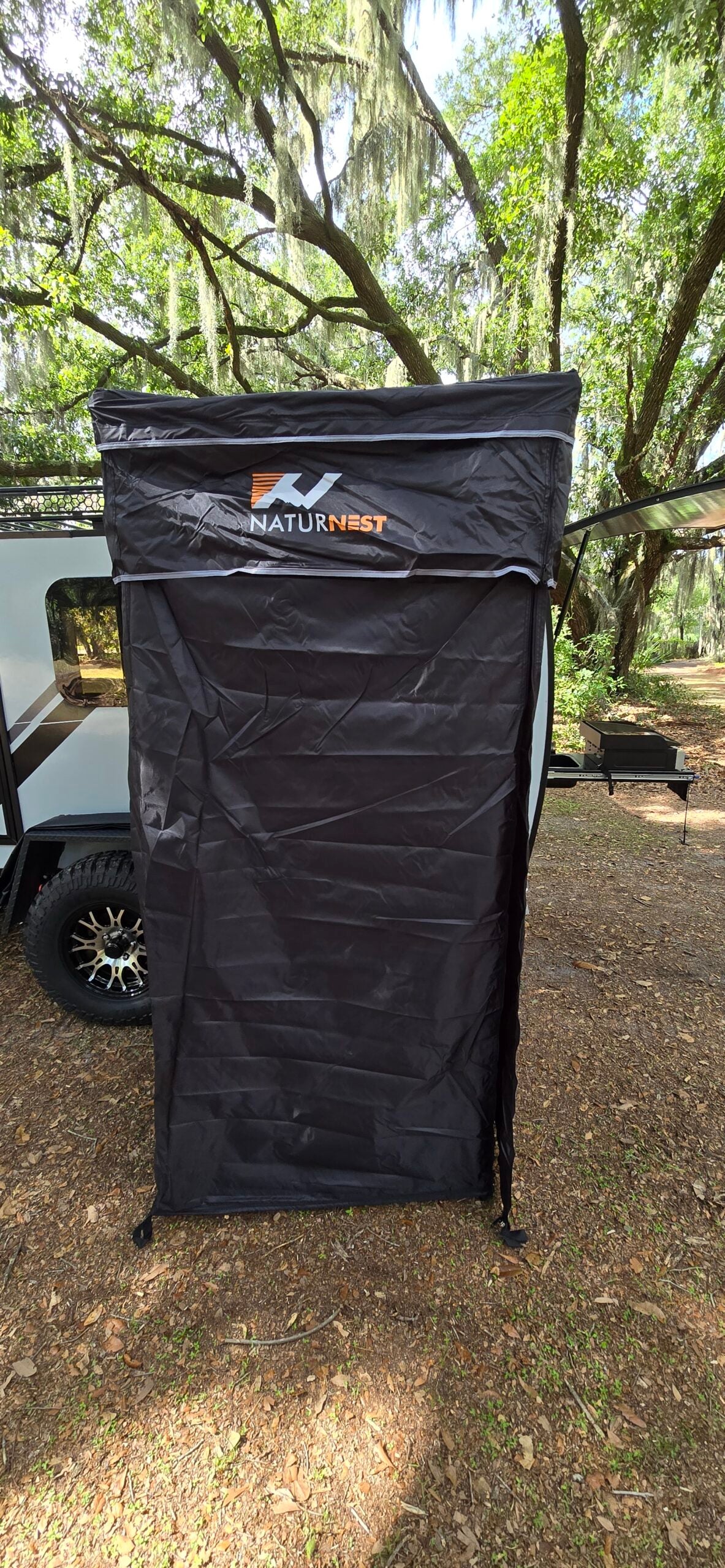 NATURNEST privacy shelter attached to an RV rental, providing outdoor changing or showering space in a wooded campsite.