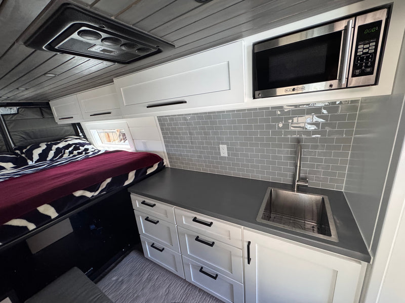  and two mountain bikes stored in the lower garage of a grey camper van.|Scenic RV rental adventure: a camper van nestled on a dirt path — photo 13