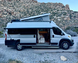 Enjoying an RV rental adventure: a silver camper van with pop-top and awning, parked amidst desert mountains.