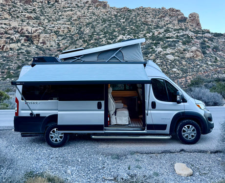 Enjoying an RV rental adventure: a silver camper van with pop-top and awning, parked amidst desert mountains.