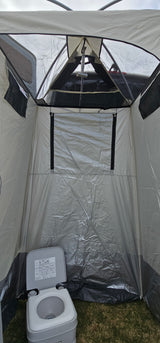 View inside a portable privacy tent with a camping toilet on grass and a shower head hanging above. Useful for RV rental.
