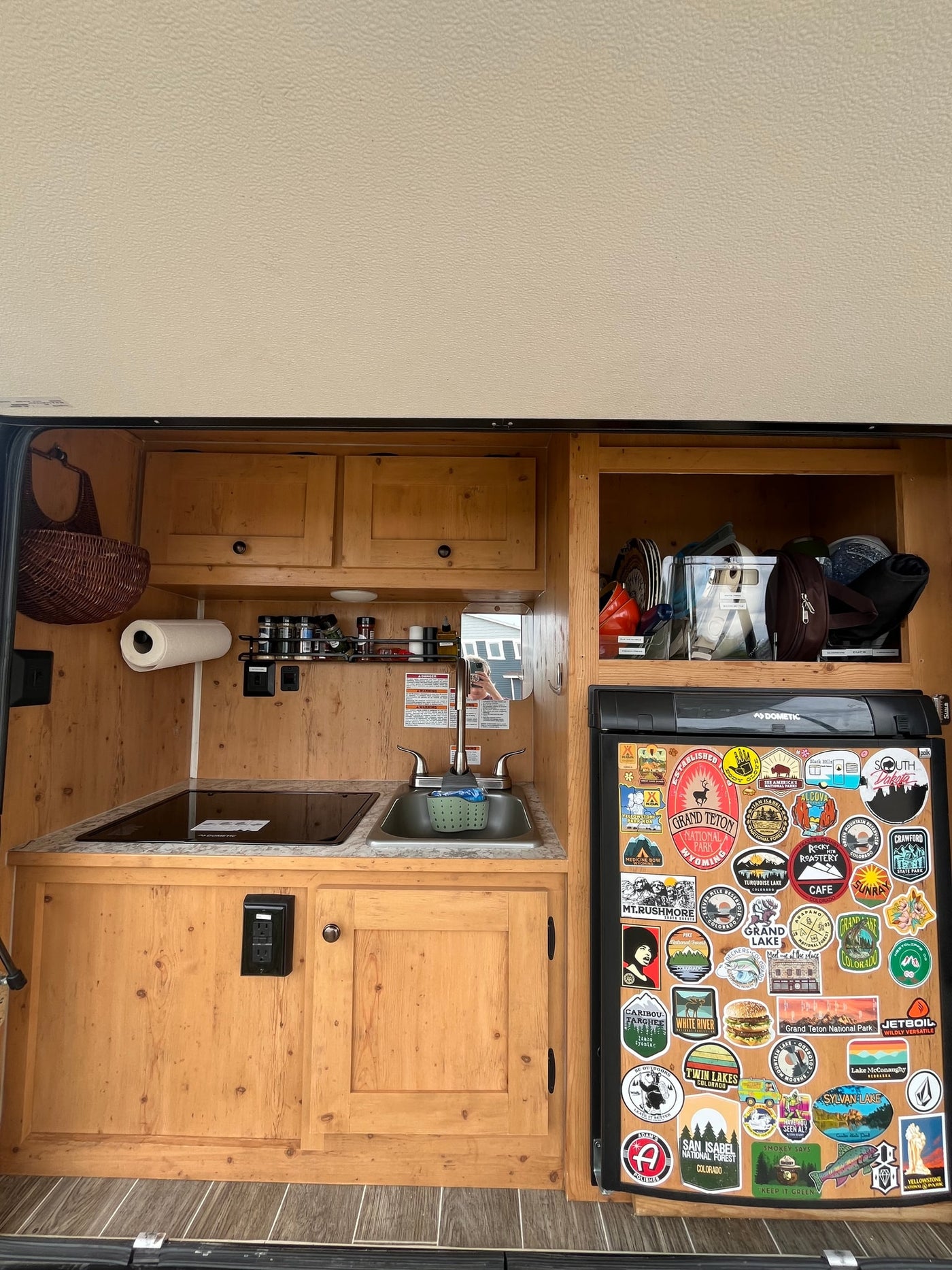 RV rental kitchen featuring light wood cabinets, a stovetop, sink, and a fridge covered in national park and travel stickers. — photo 12