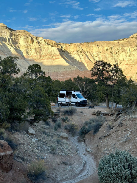 RV rental at a scenic desert campsite, nestled below towering mountains with distinctive striped rock formations under blue skies.