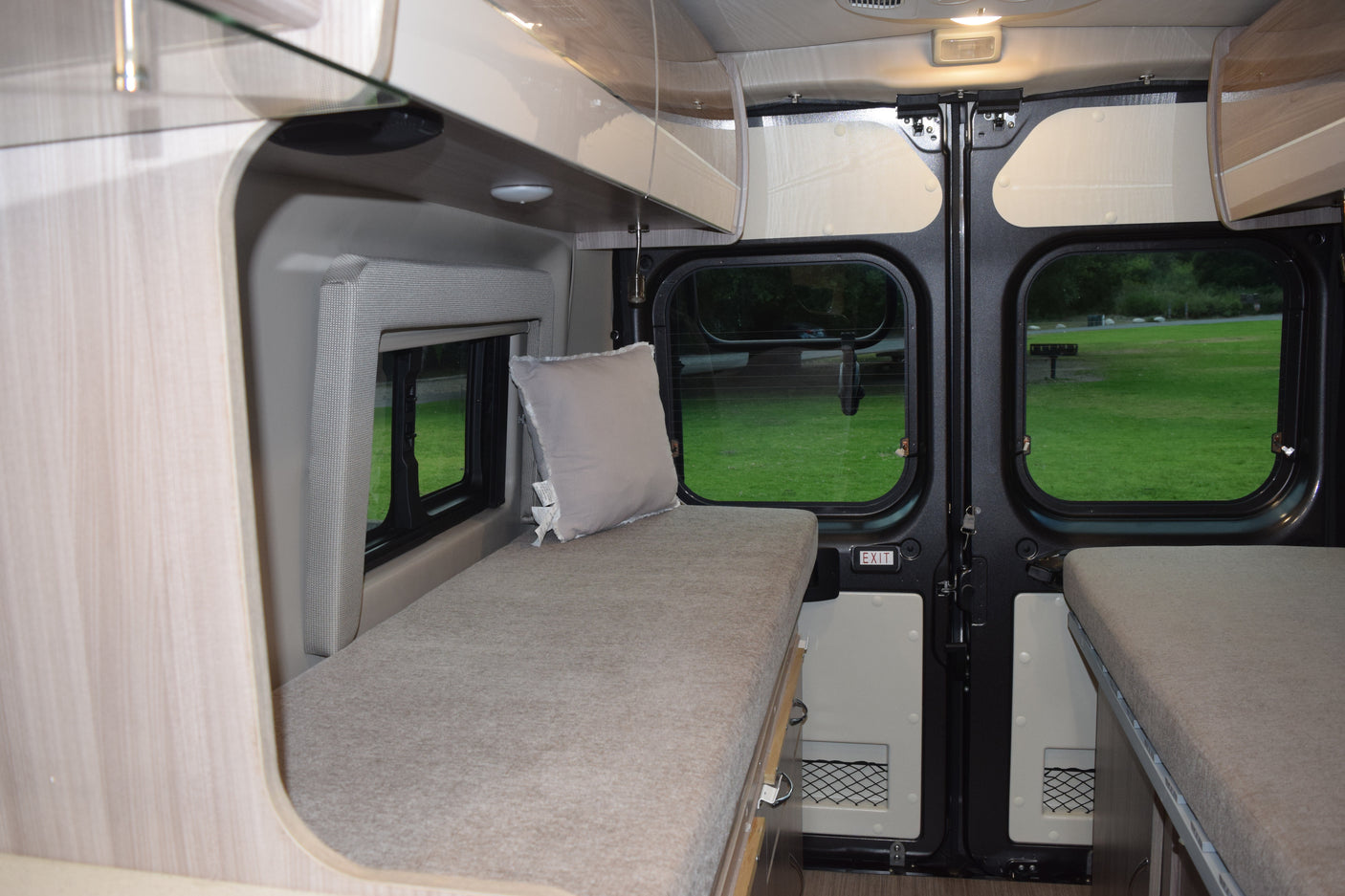 This RV rental's cozy interior features twin beds, overhead storage, and bright windows offering scenic park views for travelers.