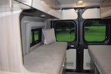 This RV rental's cozy interior features twin beds, overhead storage, and bright windows offering scenic park views for travelers.