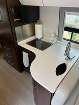 Inside a sleek **RV rental**. This compact kitchen features a modern countertop, sink, stovetop, and dark wood cabinetry.