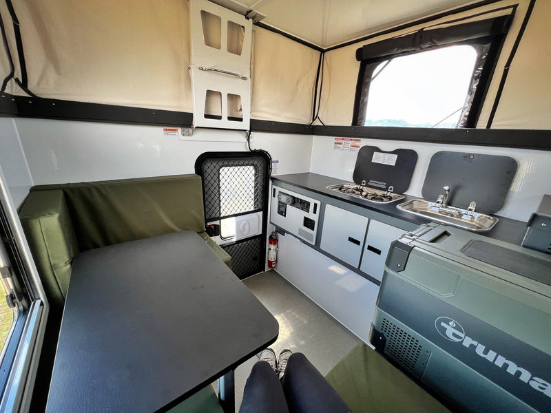Spacious RV rental interior with a kitchenette featuring a stove, sink, dinette, and a large Truma portable fridge. — photo 6