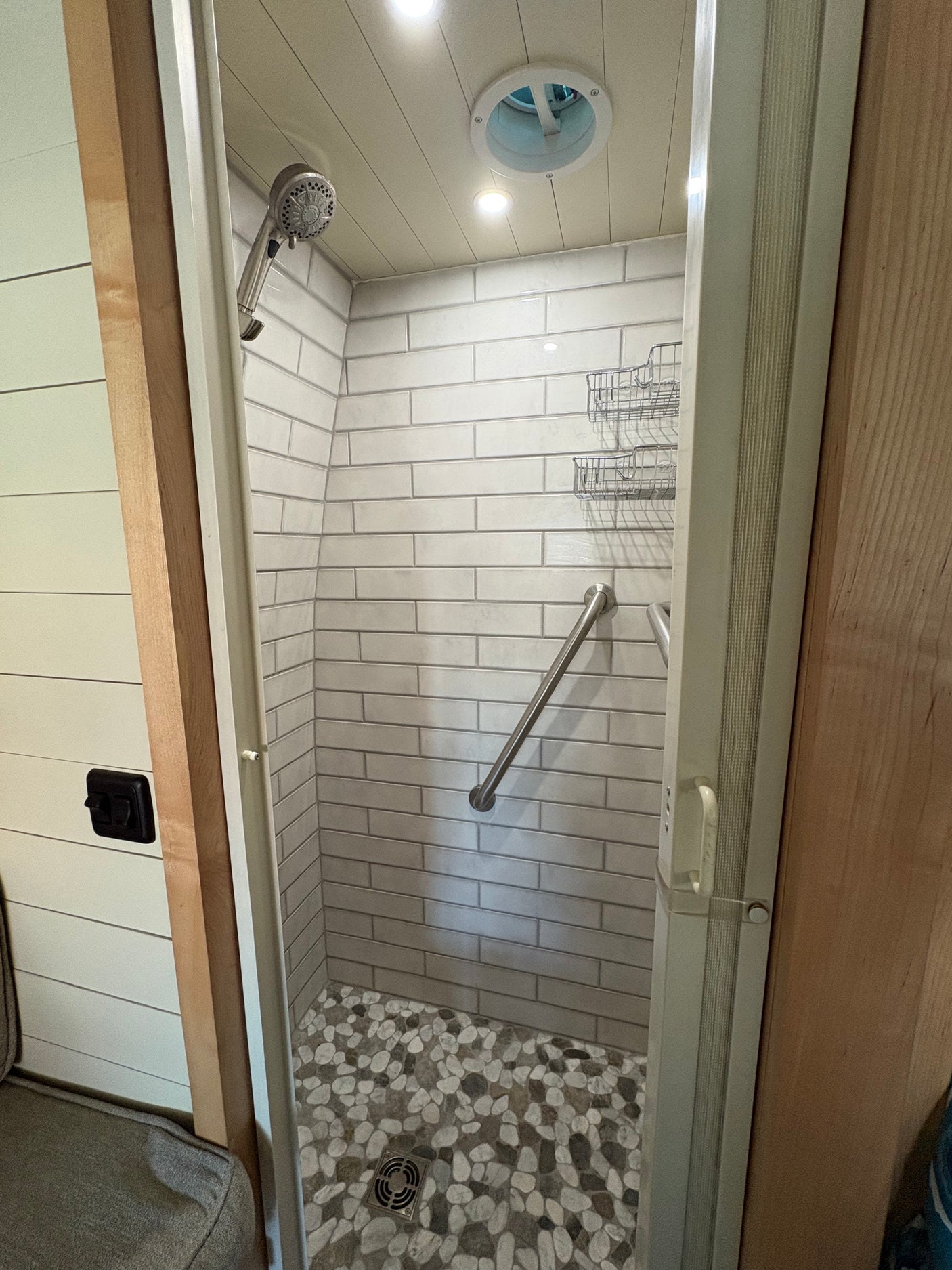 RV rental shower with sleek subway tile walls, pebble floor, grab bar, storage, and ceiling vent.