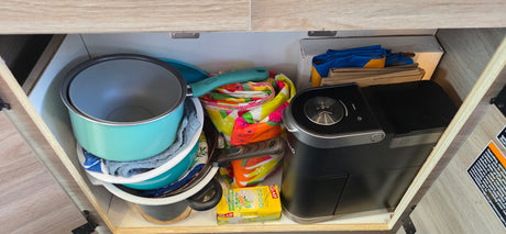 Compact kitchen cabinet in an RV rental, featuring pots, pans, coffee maker, and storage for cooking on the go.