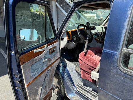 Open driver's door of a blue van, revealing the retro interior with a red seat & steering wheel. A classic rv rental option.