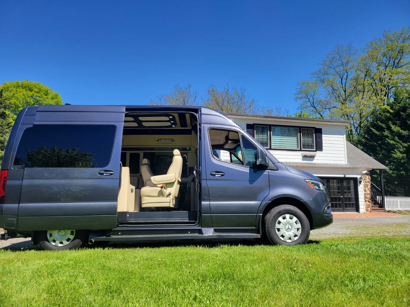 Luxury RV rental: A grey Mercedes Sprinter conversion van with open side door showing plush interior, parked on grass.
