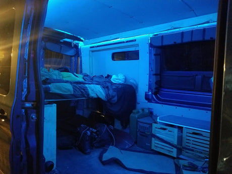 Inside a customized rv rental: ambient blue LED lights illuminate an elevated bed & practical storage crates for your adventure.