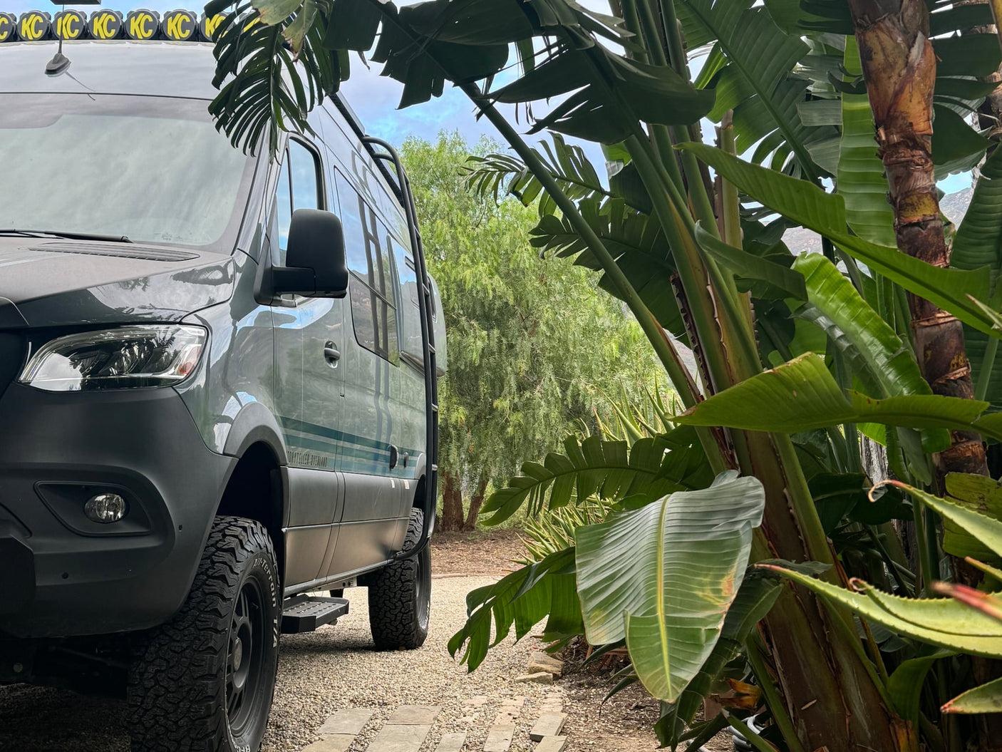  nestled among lush tropical plants.|Smiling man adjusts a foldable bed inside his RV rental