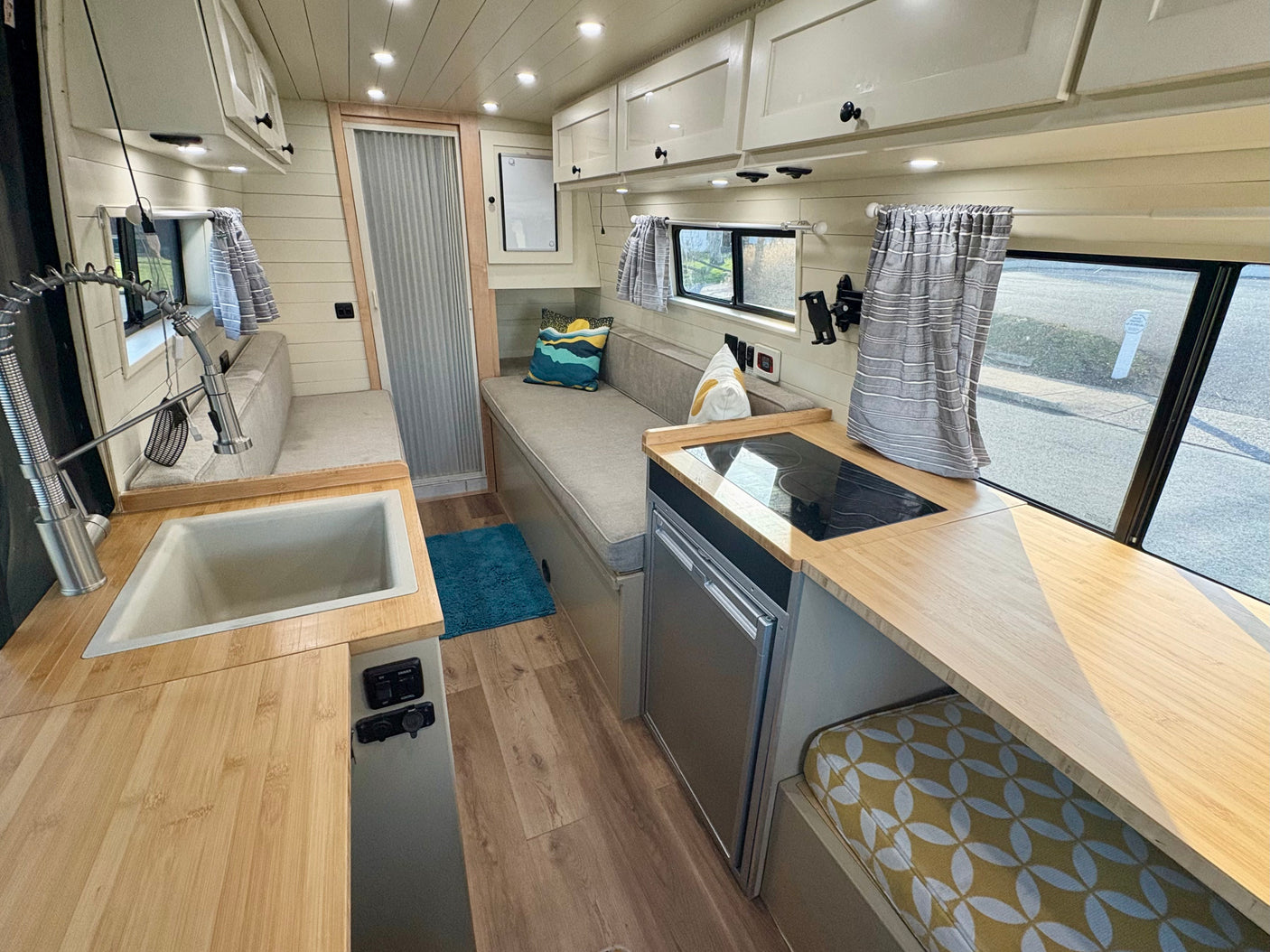Modern RV rental interior: kitchenette with induction cooktop, sink, fridge, comfy bench seating, and ample storage.
