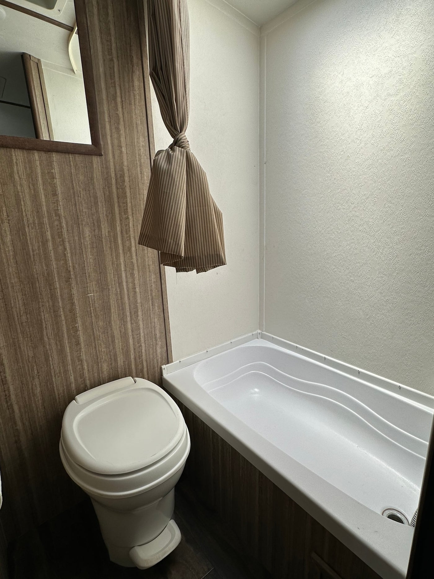 Clean RV rental bathroom featuring a compact toilet, bathtub, and tied-back shower curtain. Wood-paneled walls and a light-colored shower surround are visible. — photo 9