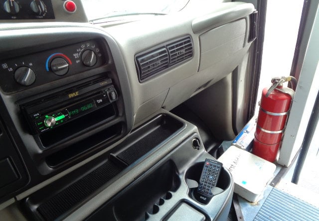  and a TV.|Inside this RV rental: multiple rows of comfortable gray seats with blue stripes and wooden consoles featuring cup holders.|Enjoy comfortable travel in this RV rental's spacious interior with striped seats — photo 6
